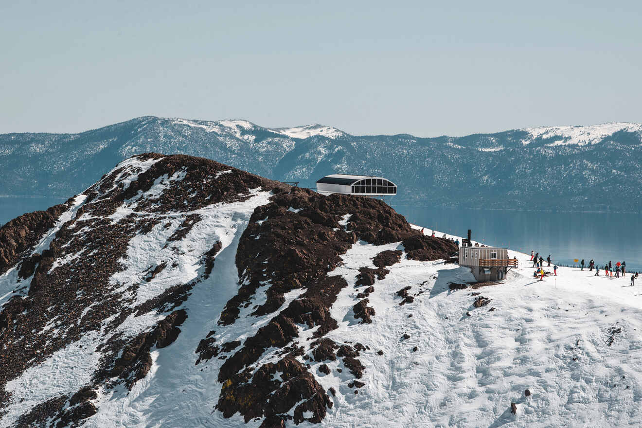 Snow-covered mountain peak with a modern observatory structure, overlooking a panoramic view with skiers.